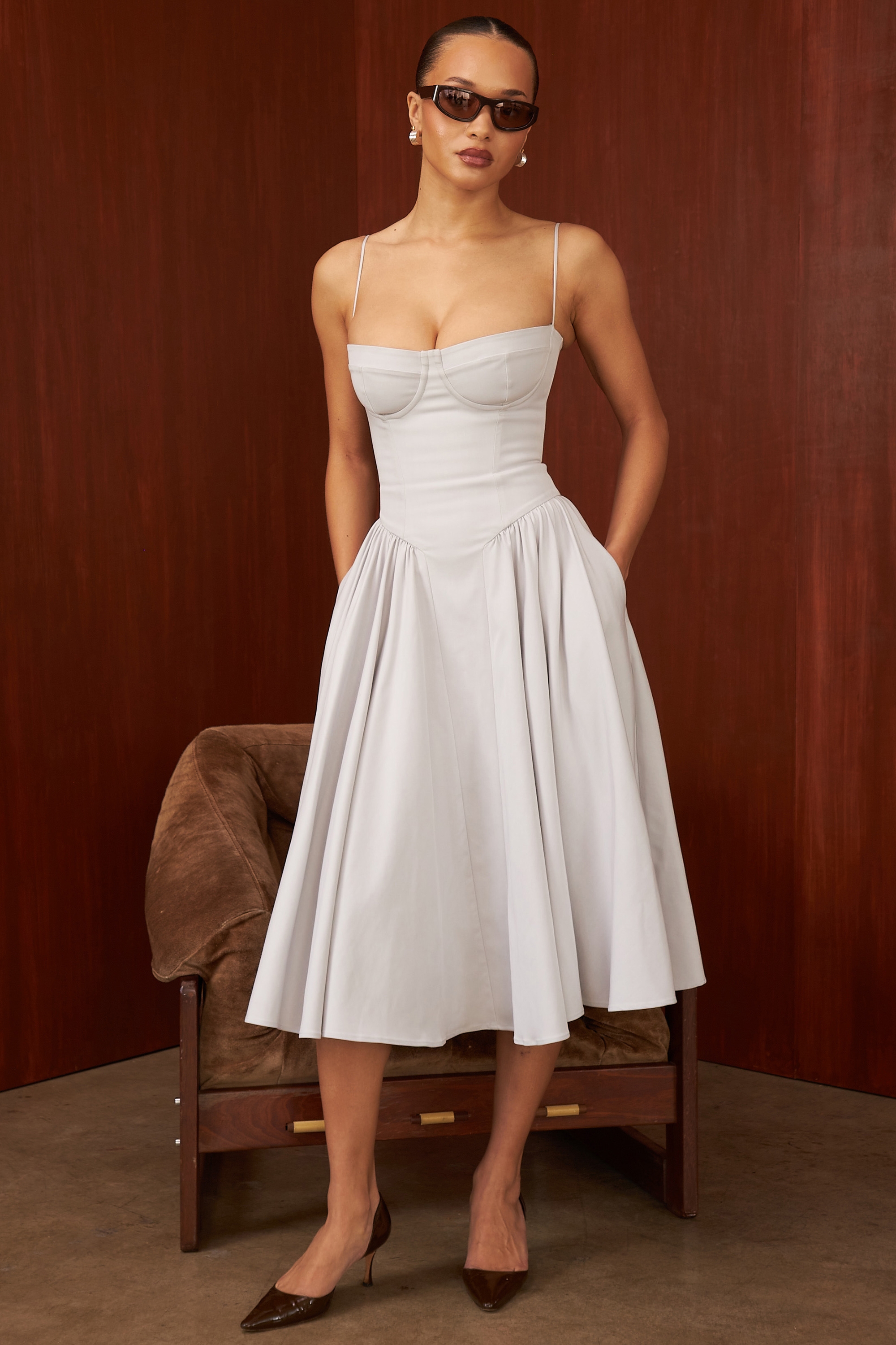 A calf-length, fitted bustier dress with a voluminous, gathered skirt. The bodice features structured three-panel bra cups and princess seams that flow into a distinctive curved waistline. The skirt's volume is created by gathered side panels inserted along a curved seam.